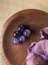 Load image into Gallery viewer, Tiny amethyst spheres in a wooden bowl next to purple silk flowers.
