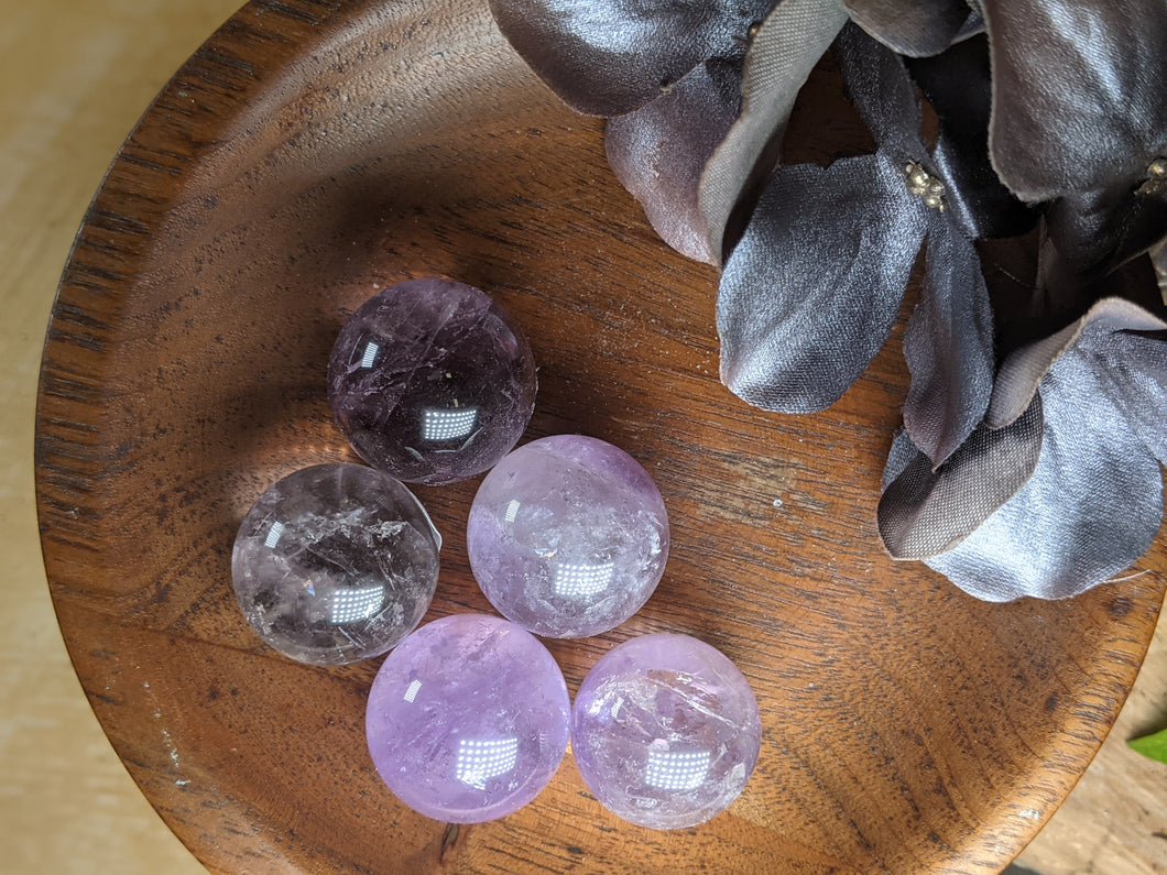 Purple amethyst spheres in a wooden bowl next to silver silk flowers