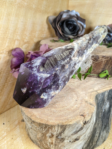 Large amethyst wand laying across two wooden stumps with periwinkle leaves and black and purple silk flowers