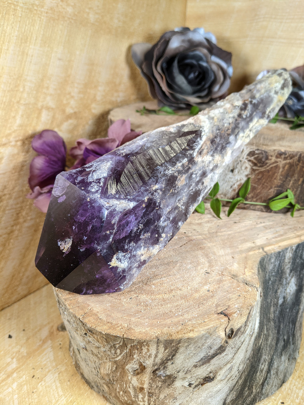 Large amethyst wand laying across two wooden stumps with periwinkle leaves and black and purple silk flowers