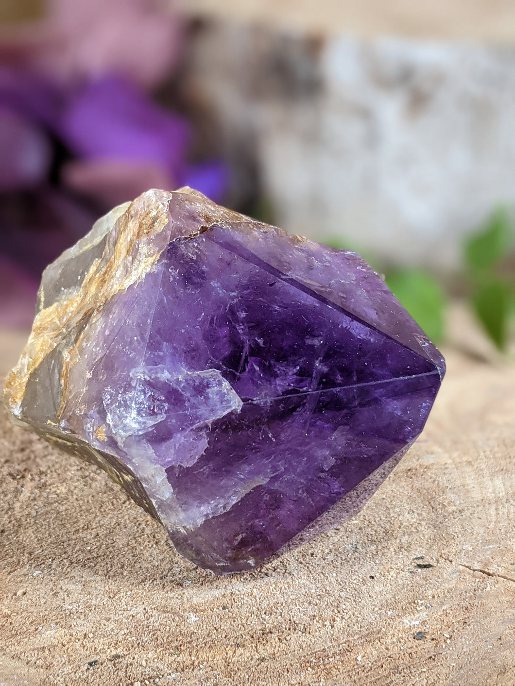 Extra small amethyst wand point laying on a wooden stump.