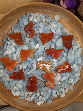 Load image into Gallery viewer, Orange carved agate fish in a bowl of aquamarine chips. 
